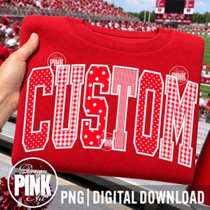 May include: A red crewneck sweatshirt featuring the word CUSTOM in large, block-style letters. Each letter has a unique white-outlined pattern, including red and white polka dots, gingham checks, and vertical stripes, set against a solid red fabric.