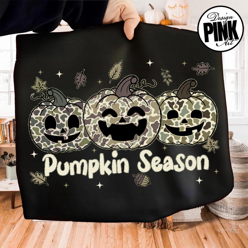 Puede incluir: Tela negra con un dise&ntilde;o que presenta tres calabazas sonrientes con un patr&oacute;n de camuflaje. Las calabazas est&aacute;n dispuestas horizontalmente y el texto "Pumpkin Season" est&aacute; debajo. Hojas y estrellas decorativas rodean las calabazas.
