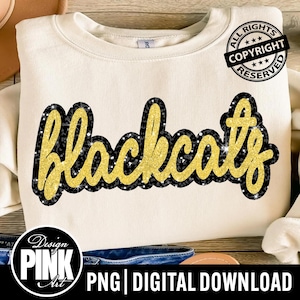 May include: Cream-colored sweatshirt with the word "Blackcats" in gold glitter lettering outlined in black and silver glitter. The design is centered on the front of the shirt. The words "Design Pink Art" are in a circle at the bottom.