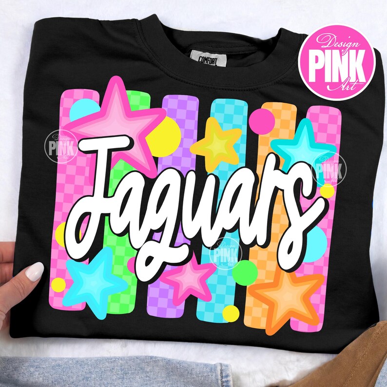 May include: Black sweatshirt with the word "Jaguars" in white script. The design includes colorful stars and vertical stripes in pink, blue, yellow, orange, and green. The words "Design Pink Art" are in a pink circle.