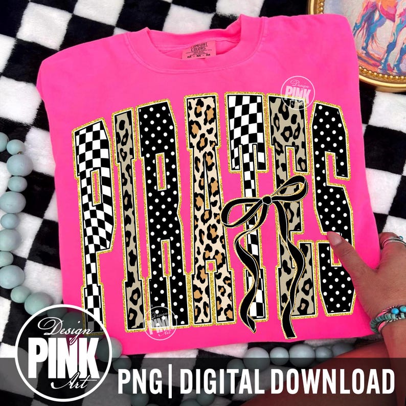 May include: A vibrant pink sweatshirt displaying the word "PIRATES" in a striking, decorative style. The letters incorporate patterns like black and white checkerboard, leopard print, and black polka dots. A black bow is at the bottom right. The text "PNG | DIGITAL DOWNLOAD" is at the bottom.