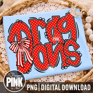 May include: A light blue t-shirt featuring the red and white polka-dotted text "drag bows" in a bold, cartoonish font. A large red and white striped bow is attached to the first letter, with black outlines surrounding the letters and the bow.