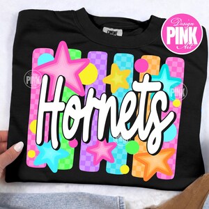 May include: Black crew neck sweatshirt with the word "Hornets" in white script. The design includes colorful stars and vertical stripes in pink, blue, yellow, and orange. The sweatshirt has a "Comfort" tag.