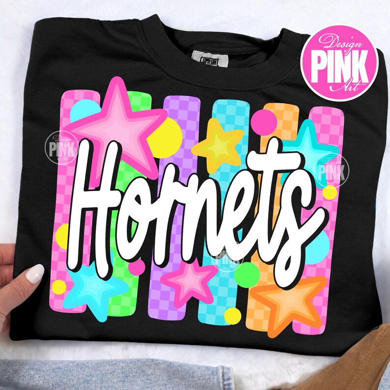 May include: Black crew neck sweatshirt with the word "Hornets" in white script. The design includes colorful stars and vertical stripes in pink, blue, yellow, and orange. The sweatshirt has a "Comfort" tag.