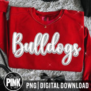 Op de afbeelding: Een felrood sweatshirt met lange mouwen en het woord Bulldogs in een wit, glinsterend, driedimensionaal cursief lettertype op de borst. Het kledingstuk heeft een ronde hals en een zichtbaar merklabel in de kraag.