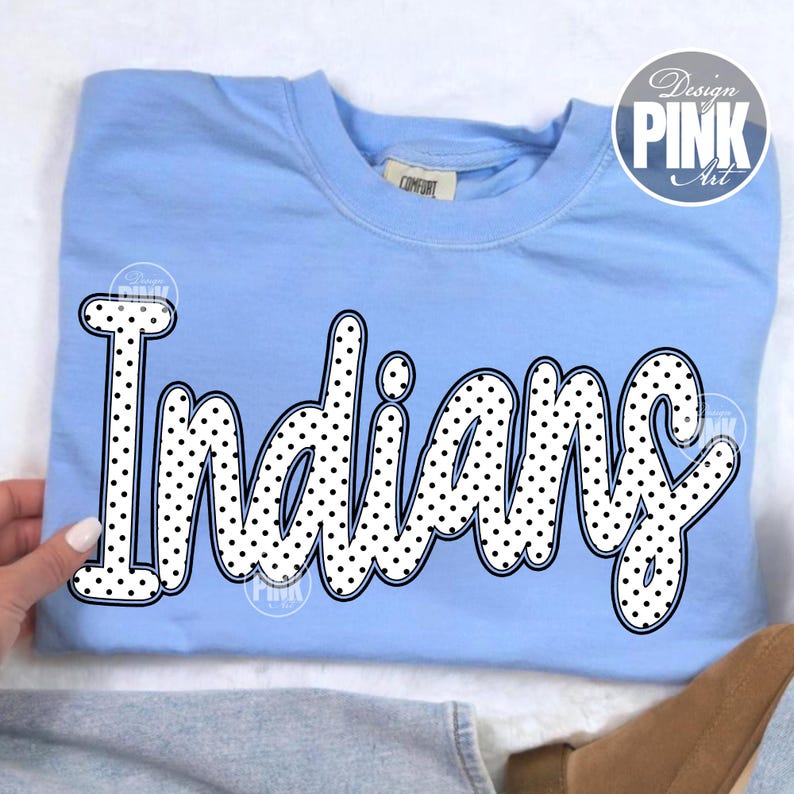 May include: A light blue sweatshirt with the word "Indians" in a black and white polka dot design. The sweatshirt has a crew neck and long sleeves. The text is in a playful, bubble-style font.
