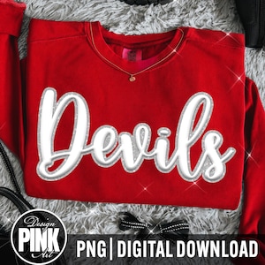 May include: A bright red crewneck sweatshirt featuring the word Devils in a large, white, cursive font with a silver glitter outline. The garment has a round neckline and long sleeves, with a visible brand tag inside the collar area.