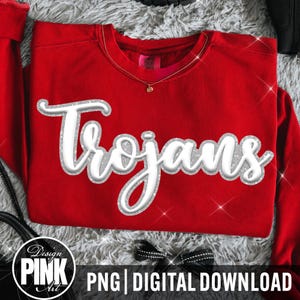 May include: A bright red crewneck sweatshirt featuring the word Trojans in a white, three-dimensional script font with a silver glitter outline. The garment has a ribbed collar and long sleeves, showcasing a bold, athletic-inspired design.