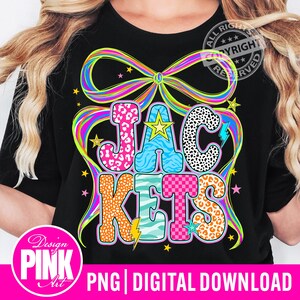 May include: Black t-shirt with the word "JACKETS" in a colorful, patterned design. The letters are in pink leopard print, blue zebra stripes, and orange leopard print. A large rainbow bow and stars surround the text.
