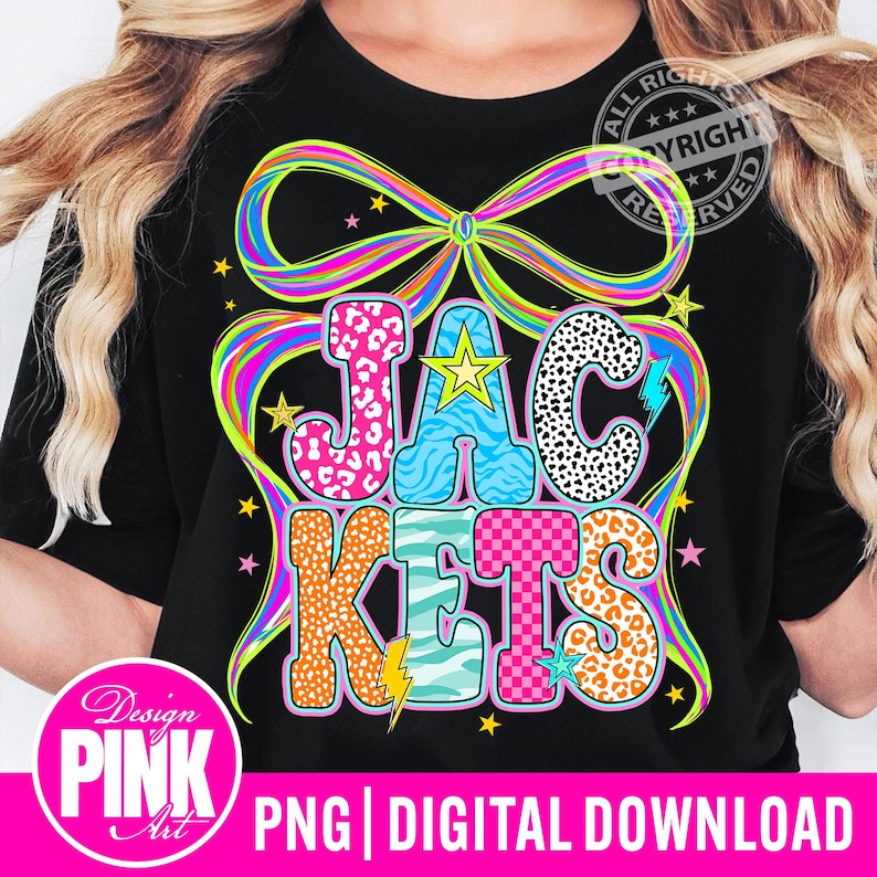 May include: Black t-shirt with the word "JACKETS" in a colorful, patterned design. The letters are in pink leopard print, blue zebra stripes, and orange leopard print. A large rainbow bow and stars surround the text.