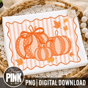 May include: A white t-shirt featuring a graphic of three orange pumpkins with white polka dots, tied with an orange ribbon. The design is set against a background of vertical light orange stripes, framed by a wavy orange border with scattered orange leaves.
