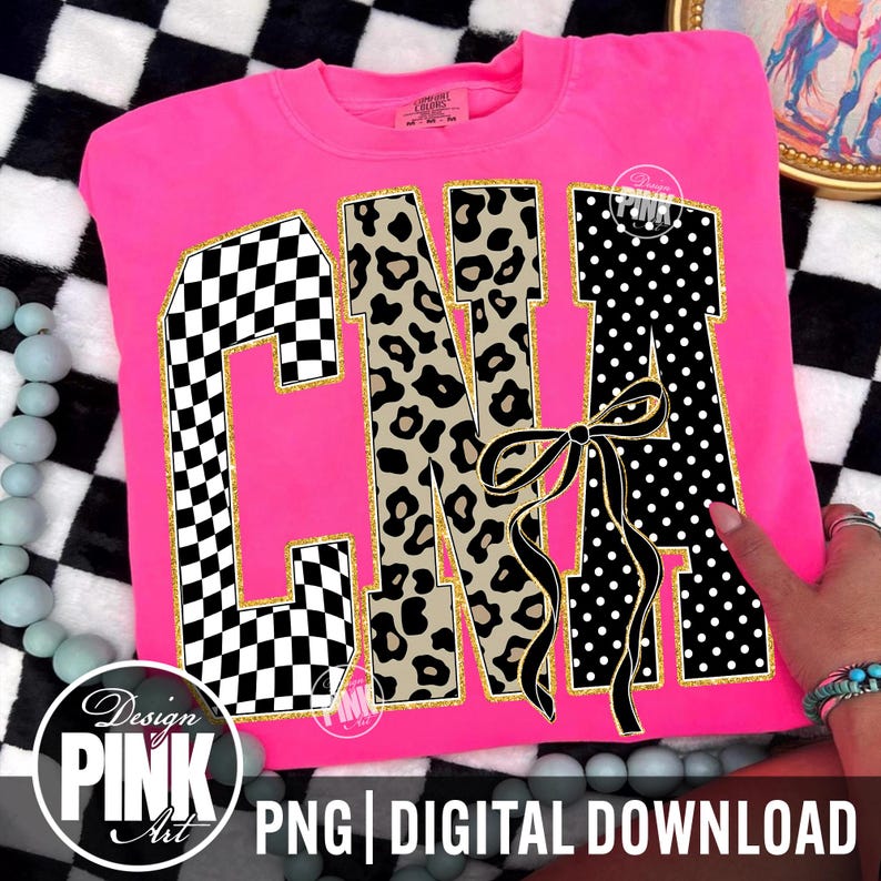 May include: A bright pink sweatshirt with the letters "CNA" in a bold design. The "C" features a black and white checkered pattern, the "N" has a leopard print, and the "A" has white polka dots. A black bow is centered below the letters.