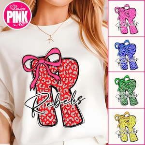 May include: White sweatshirt with a large red letter 'R' with a silver leopard print and a pink bow. The word 'Rebels' is written below in cursive. Additional images show the design with blue, green, and yellow bows. Design by Pink Art.