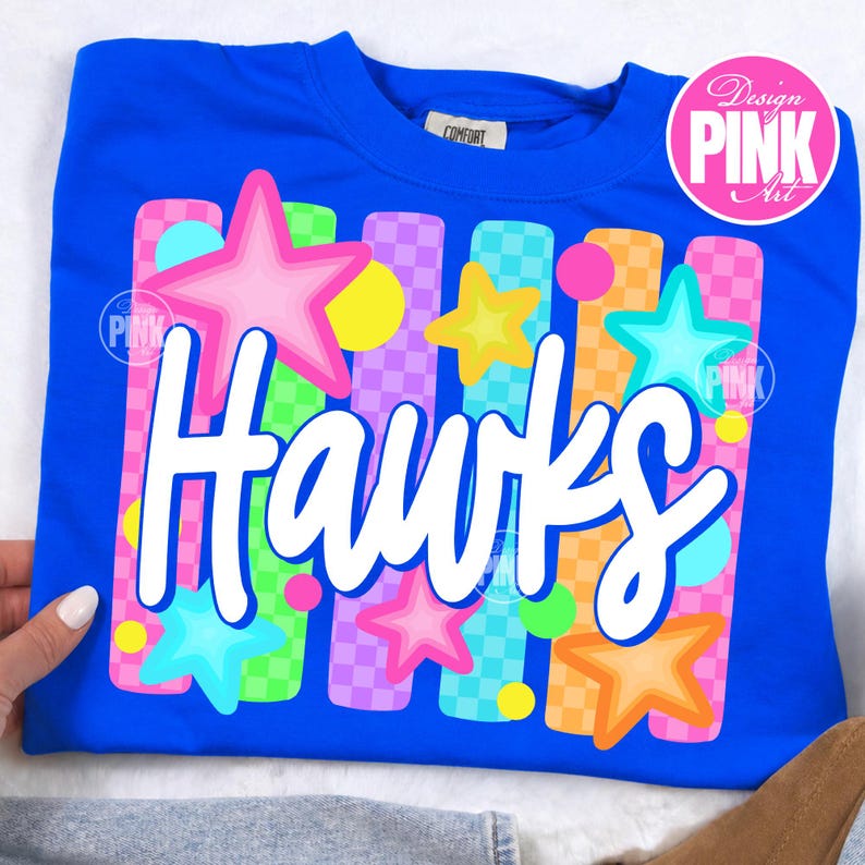 May include: A royal blue sweatshirt with the word "Hawks" in white script. The design includes colorful stars, circles, and vertical stripes in pink, yellow, green, orange, and purple. The shirt has a "Comfort" tag.