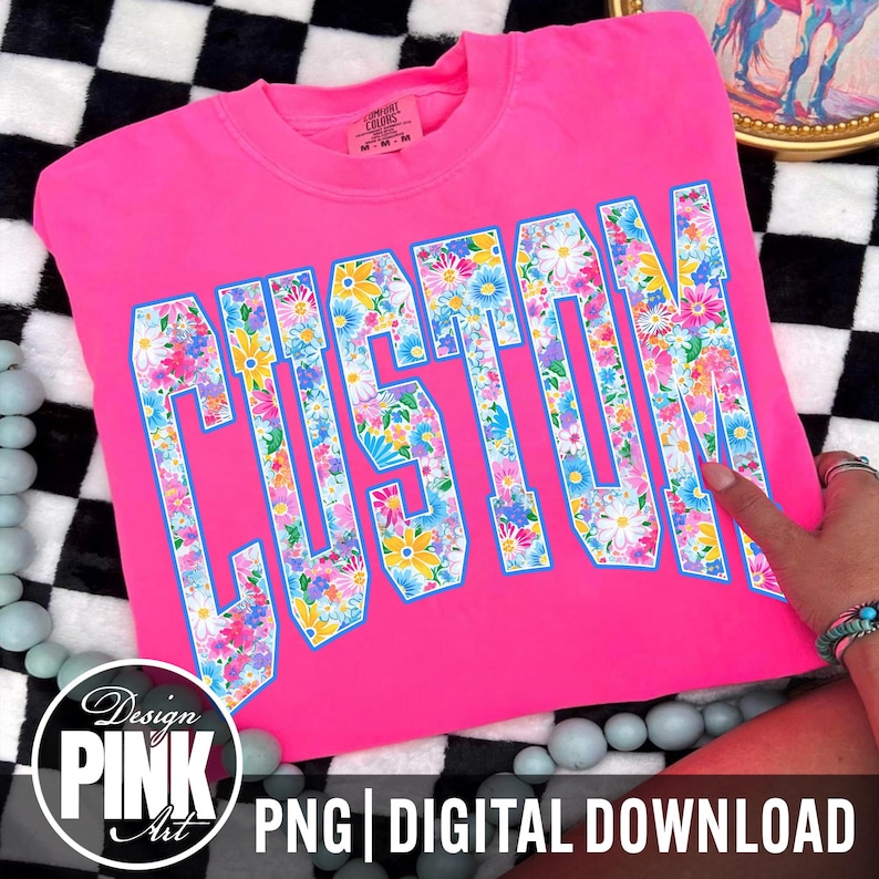 May include: A bright pink t-shirt with the word "CUSTOM" in large, floral-filled letters. The letters are outlined in blue. The shirt is displayed on a black and white checkered surface. The image also includes the text "Design PINK Art PNG DIGITAL DOWNLOAD".
