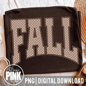 May include: A dark brown t-shirt featuring the word FALL in large, block-style letters. The letters are light tan with a white polka dot pattern and a dark brown outline. A circular logo in the bottom left corner contains the text Design PINK Art.