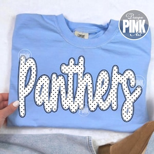 May include: Pale blue sweatshirt featuring the word "Panthers" in white, polka-dot lettering. The crew neck sweatshirt has a "Comfort" tag. A "Design Pink Art" logo is visible in the upper right corner.