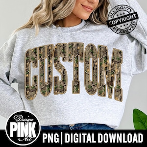 May include: A light gray sweatshirt with the word "CUSTOM" in large, block letters across the front. The letters are filled with a camouflage pattern. The design includes a "Design PINK Art" logo and the text "PNG | DIGITAL DOWNLOAD".