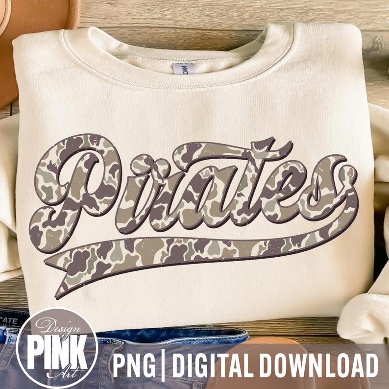 May include: Cream-colored sweatshirt with the word "Pirates" in a camouflage pattern across the front. The word is in a stylized font with a curved underline. The design includes the text "PNG | DIGITAL DOWNLOAD" and a "Design Pink Art" logo.