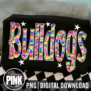May include: A black t-shirt featuring the word Bulldogs in a colorful, multi-patterned mosaic design with bright geometric shapes. The text is surrounded by small white stars. A circular logo in the corner reads Design PINK Art PNG DIGITAL DOWNLOAD.