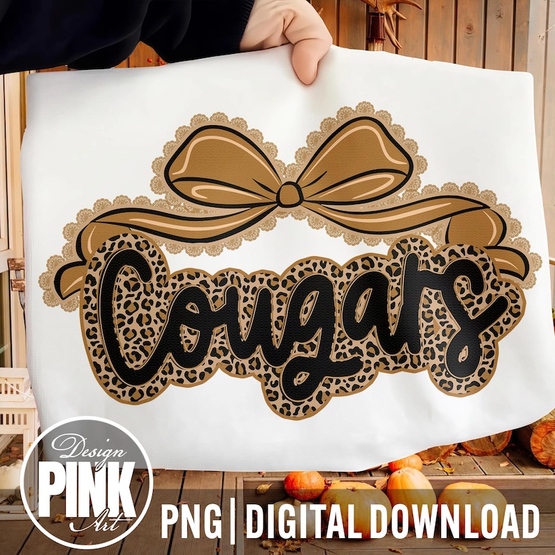 May include: White fabric with a brown bow and the word "Cougars" in a leopard print design. The design includes a decorative lace trim. The bottom of the image has the text "PNG | DIGITAL DOWNLOAD" and the words "Design PINK Art" in a circle.