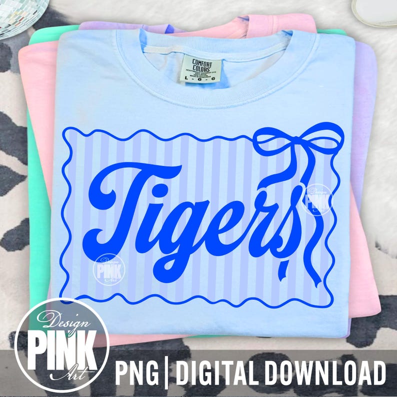 May include: A stack of pastel-colored t-shirts. The top shirt is light blue with a blue striped design and the word "Tigers" in a bold, cursive font. The design includes a bow. The bottom of the image has the text "PNG | DIGITAL DOWNLOAD".