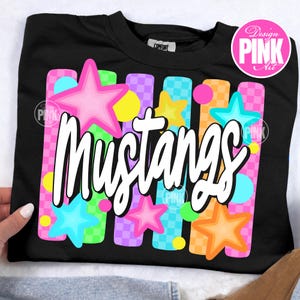 May include: Black sweatshirt with the word "Mustangs" in white script. The design includes colorful stars and vertical stripes in pink, blue, yellow, and orange. The sweatshirt has a crew neck.