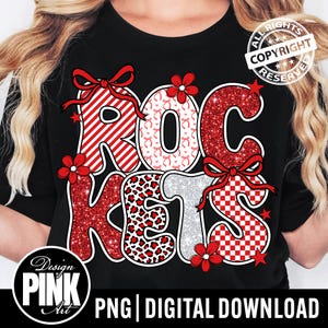May include: Black t-shirt with the word "ROCKETS" in a decorative font. The letters are in red, white, and silver with various patterns, including stripes, leopard print, and gingham. Red bows and flowers accent the letters. The shirt has a "Design Pink Art" logo.
