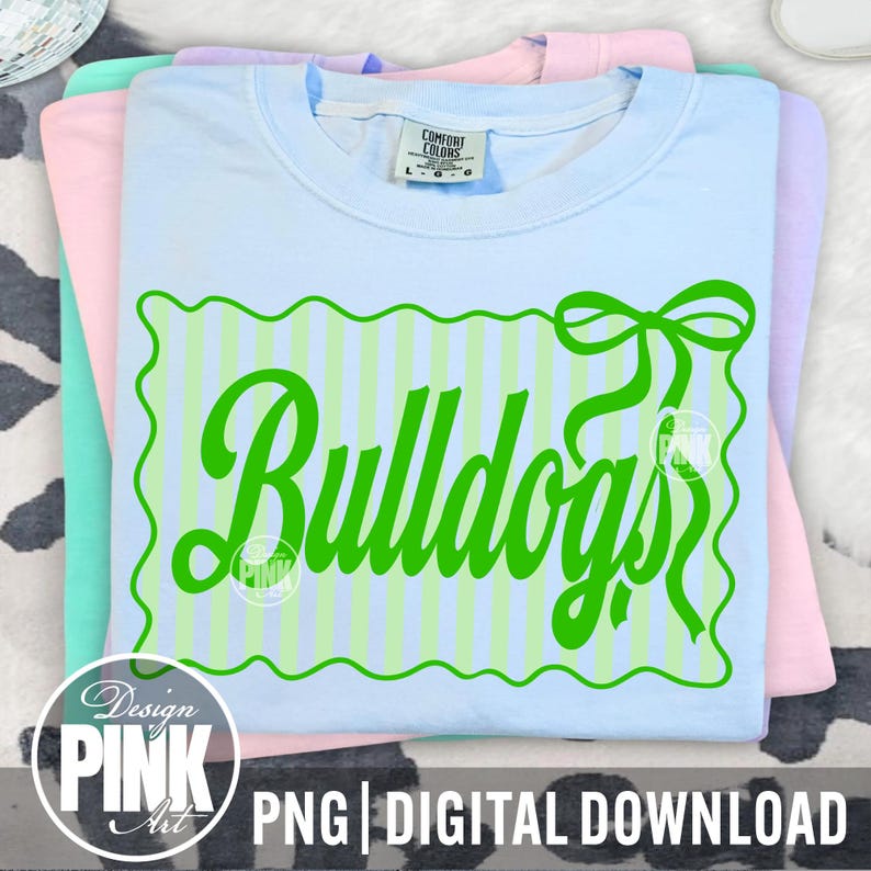 May include: A stack of pastel-colored t-shirts. The top shirt is light blue with a green design that says "Bulldogs" in a script font. The design is on a striped background with a bow. The bottom of the image says "PNG | DIGITAL DOWNLOAD".