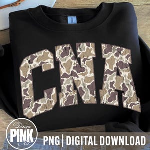 May include: Black sweatshirt with the letters "CNA" in a camouflage pattern. The letters are in a bold, collegiate-style font. The sweatshirt has a crew neck and long sleeves. The bottom of the image has the text "PNG | DIGITAL DOWNLOAD" and a logo.
