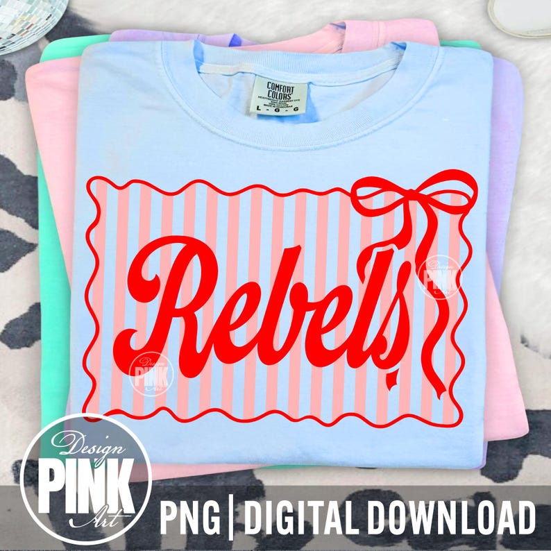 May include: A stack of pastel-colored t-shirts. The top shirt is light blue with a red design that says "Rebels" in a script font. The design is on a striped background. The shirt has a Comfort Colors tag.