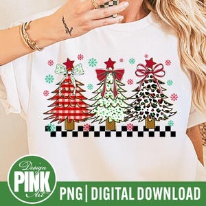 May include: White t-shirt featuring three Christmas trees with red, green, and leopard print designs. Each tree has a star on top and a bow. The shirt also has snowflakes and the text "Design Pink Art PNG Digital Download".
