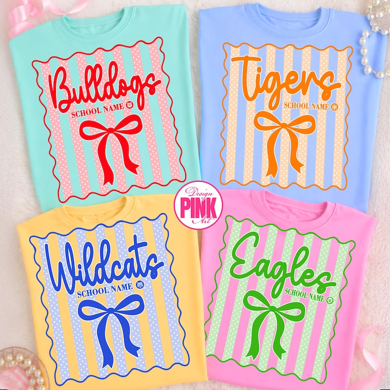 May include: Four colorful t-shirts with school mascot designs. Each shirt features a team name in a script font, a bow, and vertical stripes. The shirts are light blue, yellow, pink, and blue.