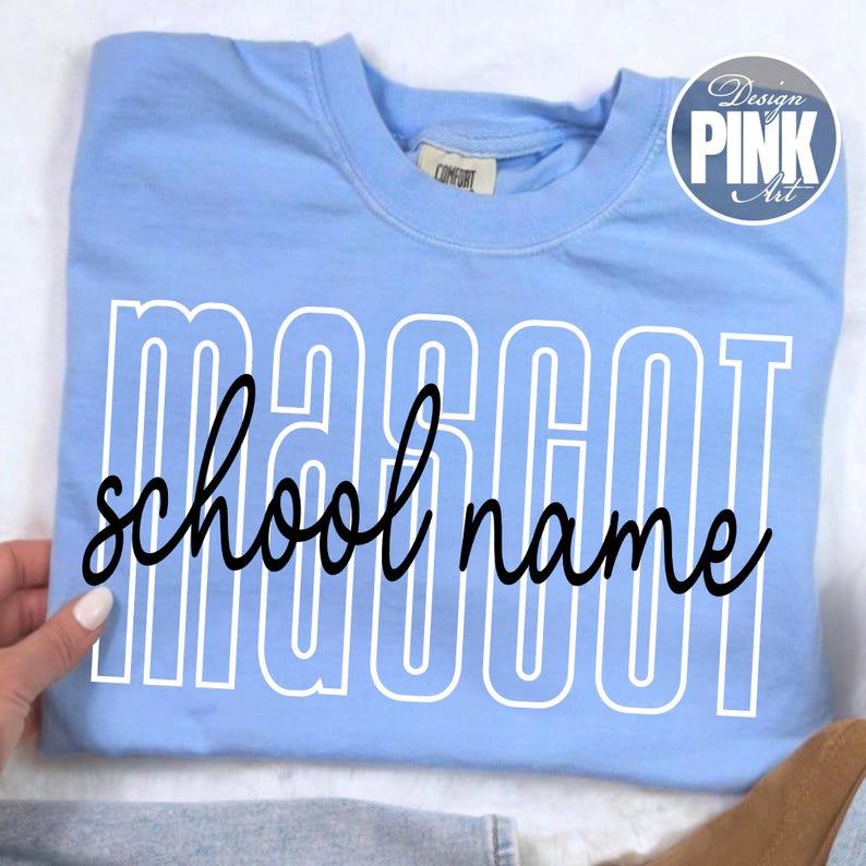 K&ouml;nnte beinhalten: Hellblaues Sweatshirt mit dem Wort "MASCOT" in wei&szlig;en Blockbuchstaben und "school name" in schwarzer Schreibschrift. Das Sweatshirt hat ein "Design Pink Art" Logo in der oberen rechten Ecke.