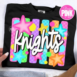 May include: Black crew neck sweatshirt with the word "Knights" in white script. The design includes colorful stars, circles, and checkered stripes in pink, blue, yellow, and orange. The sweatshirt has a "Comfort" tag.