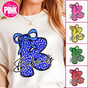 May include: White sweatshirt with a large blue letter "R" in a leopard print design and a blue bow. The word "Bobcats" is written below in a script font. Additional images show the design in pink, yellow, green, and red.