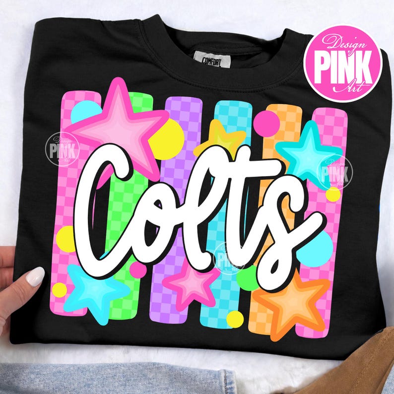 Pu&ograve; includere: Felpa nera con la scritta "Colts" in corsivo bianco. Il design include stelle colorate e strisce verticali rosa, verdi, arancioni e viola, con un motivo a scacchi. La felpa ha uno scollo tondo.