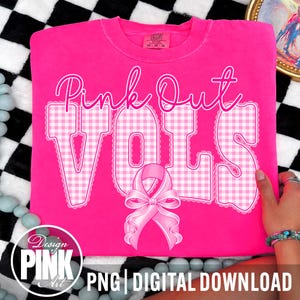 Op de afbeelding: Een felroze t-shirt met de tekst Pink Out VOLS in een wit gingham-patroon met kanten randen. Onder de tekst staat een grote, gedetailleerde roze bewustwordingslint met een strik. Het shirt heeft een ronde hals en een Comfort Colors label.