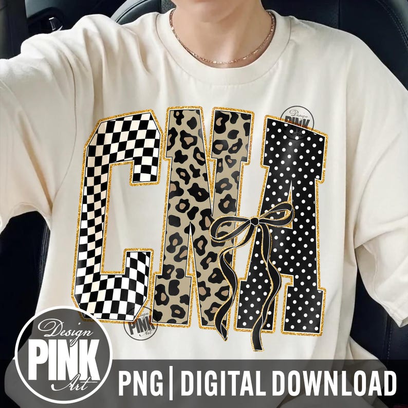 May include: Cream-colored t-shirt featuring the letters "CMA" in a bold, decorative style. The "C" has a black and white checkered pattern, the "M" has a leopard print, and the "A" has white polka dots. A black bow is centered on the design.