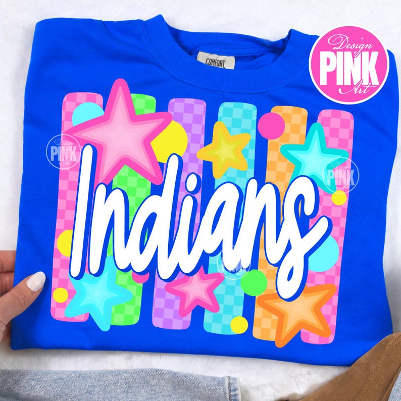 May include: A royal blue crew neck sweatshirt with the word "Indians" in white script. The design includes colorful stars and vertical stripes in pink, green, orange, and purple. The shirt has a "Design PINK Art" logo.