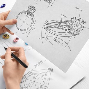 May include: A jewelry designer's hand sketches of diamond rings and other jewelry pieces. The designs are detailed with measurements, including an 8x6mm stone and a 14x17mm stone. Colored gemstones are scattered around the sketches.