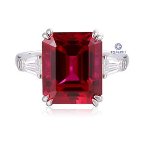 Pode incluir: Um anel deslumbrante com uma grande pedra preciosa retangular vermelha escura. O anel tem uma banda prateada e &eacute; ladeado por duas pedras preciosas claras retangulares menores. O anel est&aacute; sobre um fundo branco.