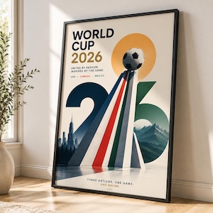以下が含まれることがあります： 2026年ワールドカップの額入りポスター。赤、白、緑のストライプが入った三角形の構造物の上にサッカーボールが描かれています。テキストは「WORLD CUP 2026, UNITED BY PASSION. INSPIRED BY THE GAME. USA, CANADA, MEXICO, THREE NATIONS. ONE GAME. ONE DREAM.」と書かれています。
