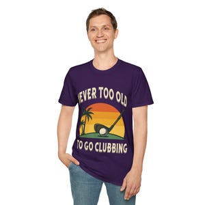 May include: A purple t-shirt with the text "NEVER TOO OLD TO GO CLUBBING" in white. The graphic features a golf club, ball, palm trees, and a sunset design. The shirt is made of a soft material.