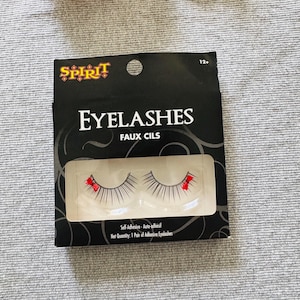 May include: Black package of faux eyelashes with the word "EYELASHES" in large white letters. The package also includes the brand name "SPIRIT" in red and gold. The eyelashes are black with red accents.