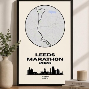 Pode incluir: Pôster emoldurado com um mapa de Leeds, Inglaterra, dentro de um círculo. O texto "LEEDS MARATHON 2026" está abaixo do mapa, com uma silhueta do horizonte da cidade. A data é 10/05/26, e a distância é 42,195 quilômetros.
