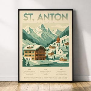 May include: A framed poster featuring a vintage travel advertisement for St. Anton, Austria. The illustration depicts snow-covered mountains, alpine houses, and a church. Text includes "ST. ANTON AUSTRIA" and phrases like "See", "Sip", and "Eat".