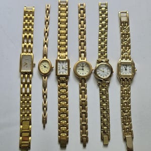May include: A collection of six gold-tone wristwatches with metal link bracelets. The watches feature various face shapes including rectangular, oval, and round, with analog displays showing Roman or Arabic numerals and the brand names Fossil, Guess, and Timex.