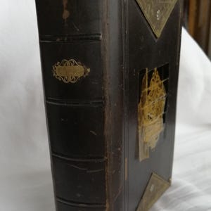 May include: A dark brown leather-bound book with gold accents. The book has a decorative gold label that reads "Columbia". The cover features a gold-colored flap and corner protectors.