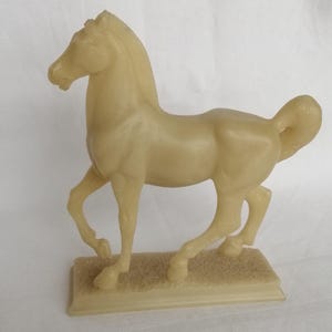 Peut inclure: Figurine de cheval crème en mouvement. Le cheval est monté sur une base rectangulaire avec une surface texturée. La figurine présente une finition lisse et des détails.